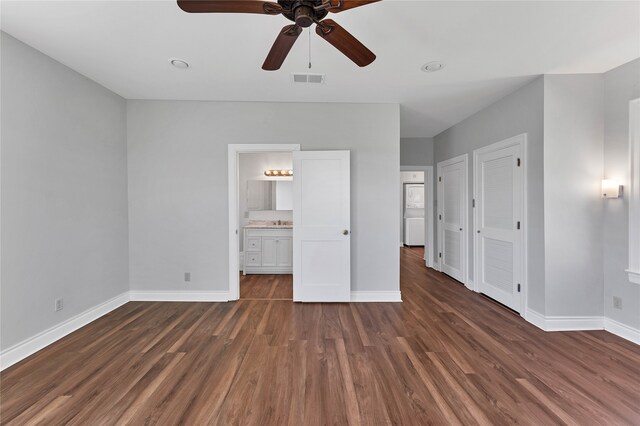 unfurnished bedroom featuring two closets, dark hardwood / wood-style flooring, ceiling fan, and ensuite bathroom