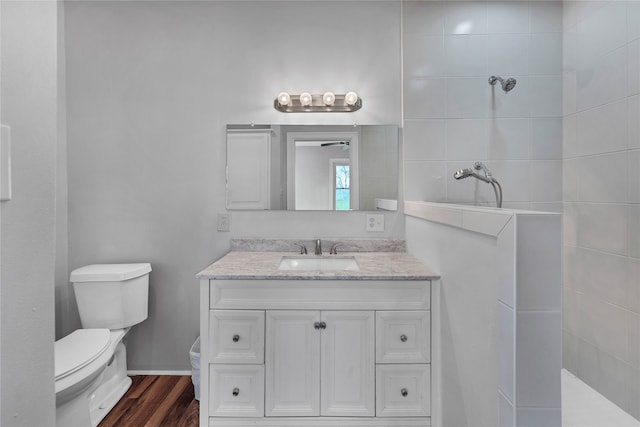 bathroom featuring toilet, a tile shower, vanity, and wood-type flooring