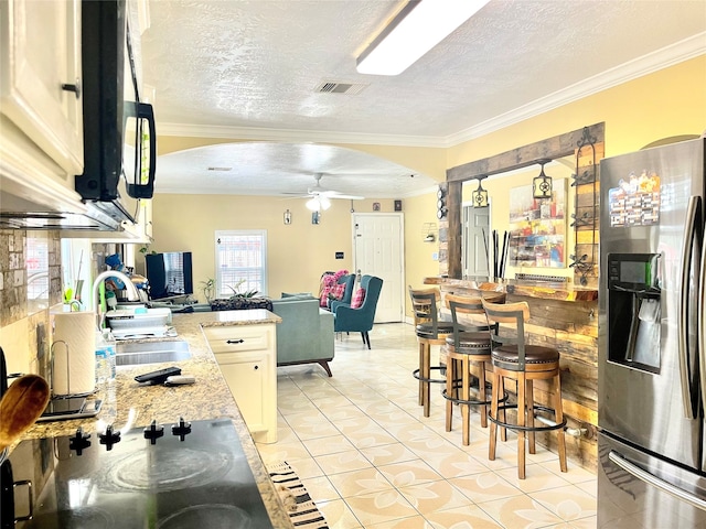 kitchen featuring ceiling fan, a textured ceiling, sink, stainless steel fridge with ice dispenser, and ornamental molding