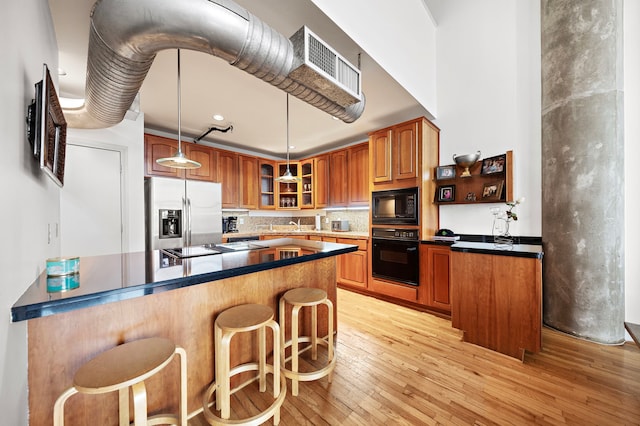 kitchen with light hardwood / wood-style flooring, hanging light fixtures, black appliances, and a breakfast bar