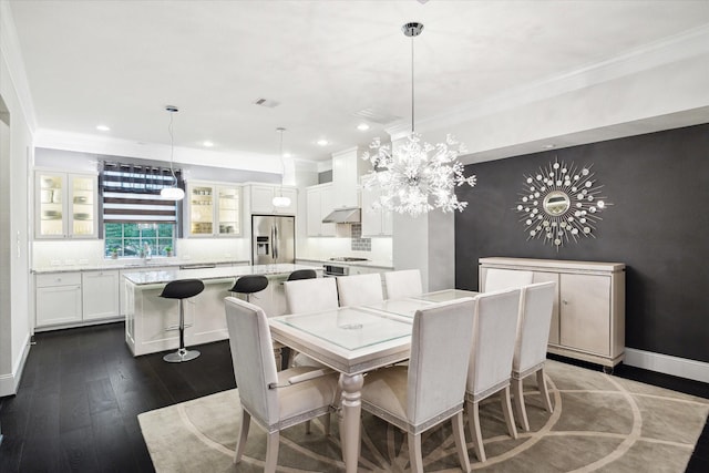 dining room with dark wood-type flooring, ornamental molding, a chandelier, and sink