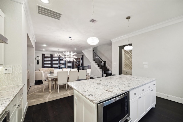 kitchen with white cabinetry, stainless steel microwave, ornamental molding, and decorative light fixtures