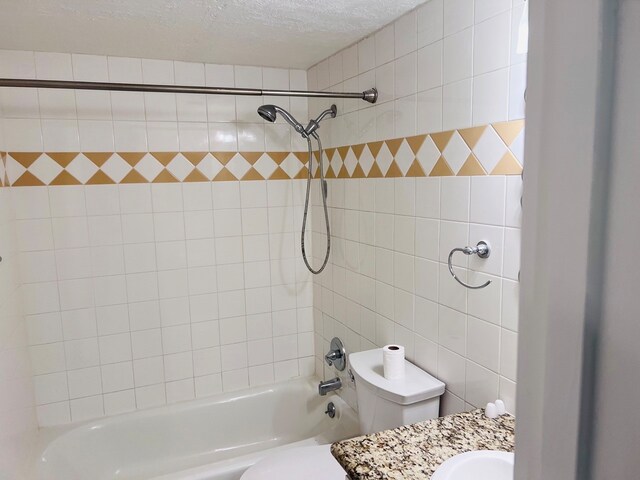 full bathroom with toilet, vanity, tiled shower / bath, a textured ceiling, and tile walls