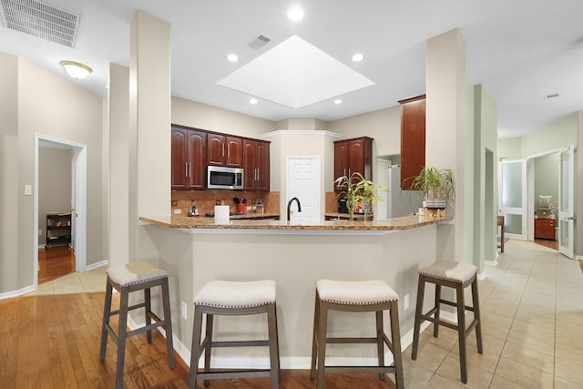 kitchen featuring a skylight, kitchen peninsula, light tile floors, and a breakfast bar area