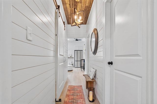 hall featuring wooden ceiling, an inviting chandelier, light wood-type flooring, and a barn door