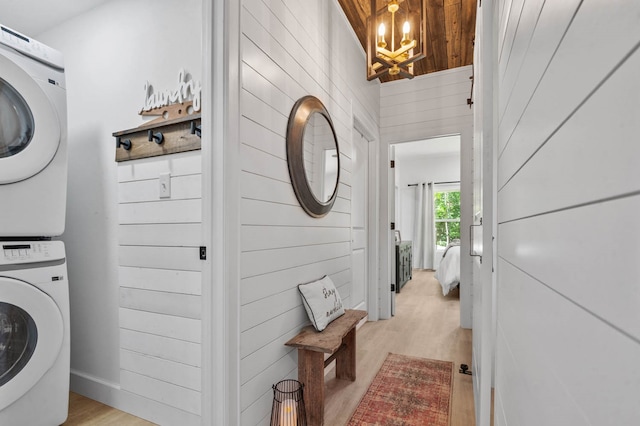 laundry room with an inviting chandelier, light hardwood / wood-style floors, and stacked washing maching and dryer