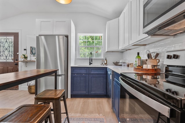 kitchen featuring appliances with stainless steel finishes, lofted ceiling, backsplash, sink, and light hardwood / wood-style flooring