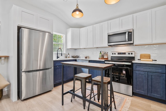 kitchen featuring backsplash, appliances with stainless steel finishes, decorative light fixtures, lofted ceiling, and light wood-type flooring