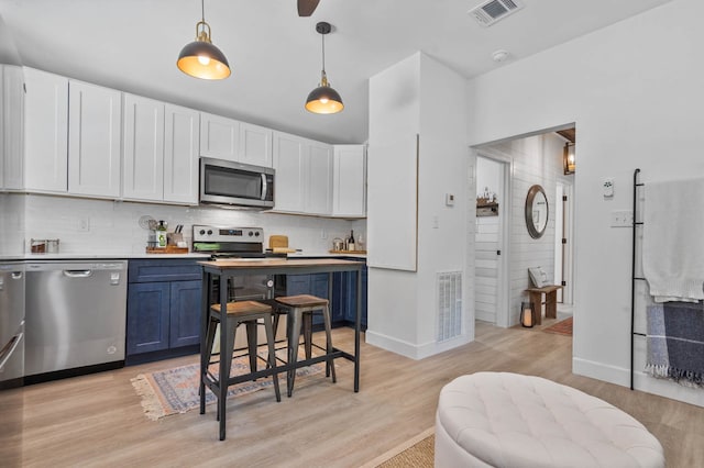 kitchen featuring appliances with stainless steel finishes, hanging light fixtures, light wood-type flooring, and blue cabinetry