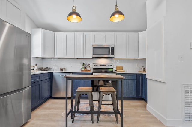 kitchen with appliances with stainless steel finishes, hanging light fixtures, light hardwood / wood-style floors, and blue cabinetry