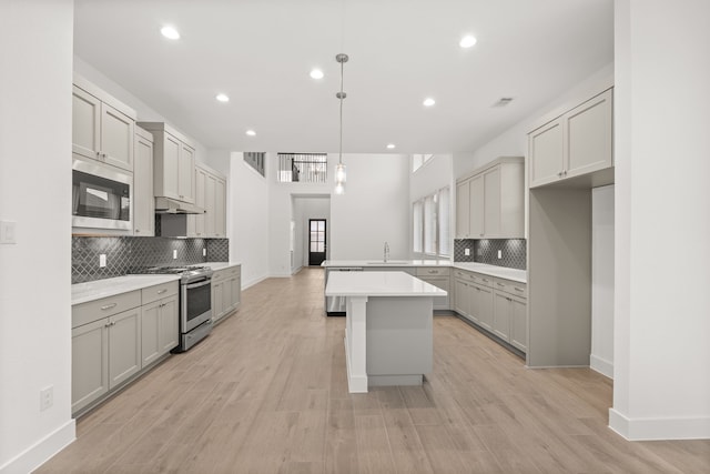 kitchen with stainless steel appliances, sink, a kitchen island, pendant lighting, and gray cabinetry