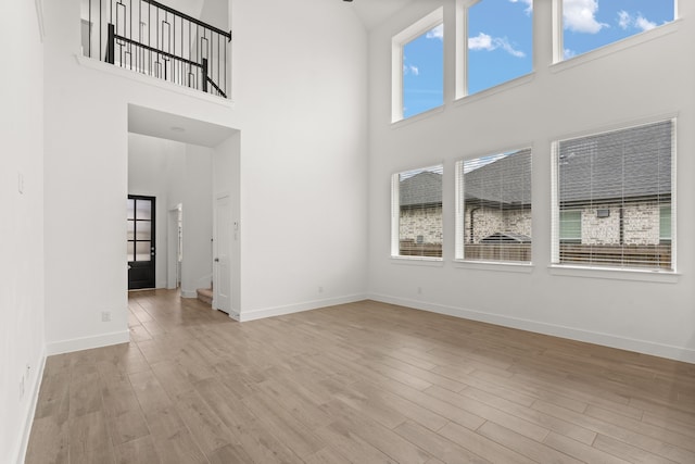 unfurnished living room with light hardwood / wood-style floors and a towering ceiling