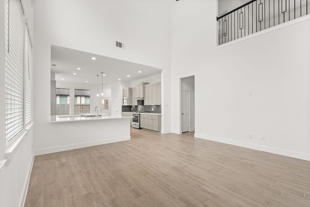 unfurnished living room with a high ceiling, light hardwood / wood-style flooring, and sink