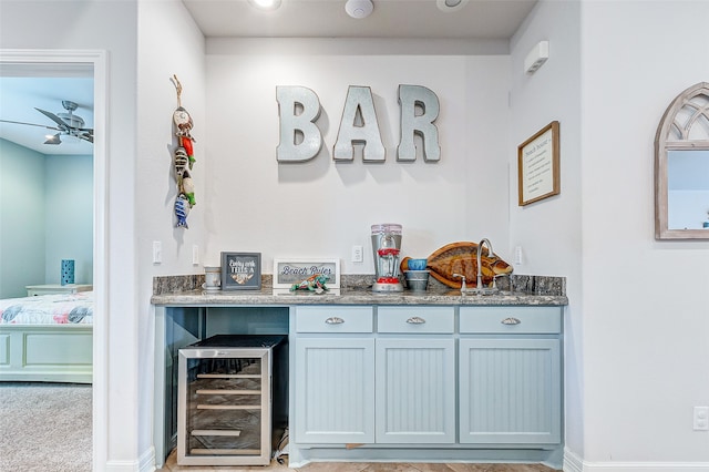 bar featuring light carpet, dark stone countertops, gray cabinets, beverage cooler, and ceiling fan