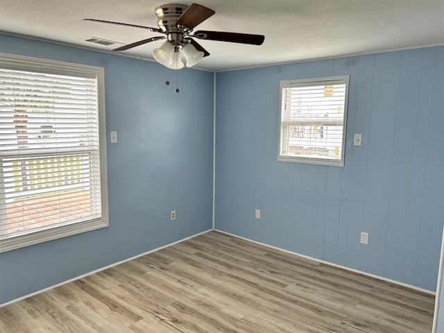 unfurnished room featuring visible vents, a textured ceiling, light wood-type flooring, and a ceiling fan