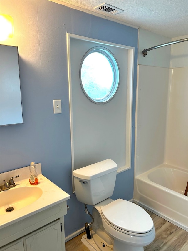 bathroom featuring visible vents, toilet, a textured ceiling, wood finished floors, and bathing tub / shower combination