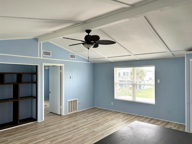 empty room with lofted ceiling with beams, wood finished floors, and visible vents