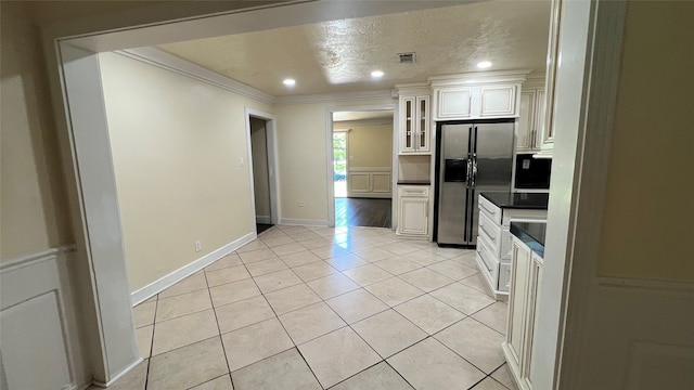 kitchen with white cabinetry, ornamental molding, light tile flooring, and stainless steel refrigerator with ice dispenser