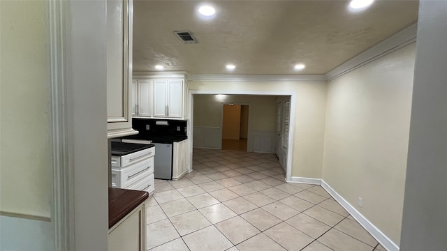 kitchen with white cabinetry, ornamental molding, light tile flooring, and stainless steel dishwasher