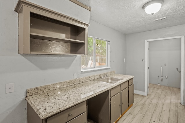 kitchen with sink, light hardwood / wood-style floors, light stone countertops, and a textured ceiling