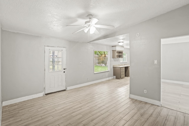 empty room with ceiling fan, light wood-type flooring, and a textured ceiling