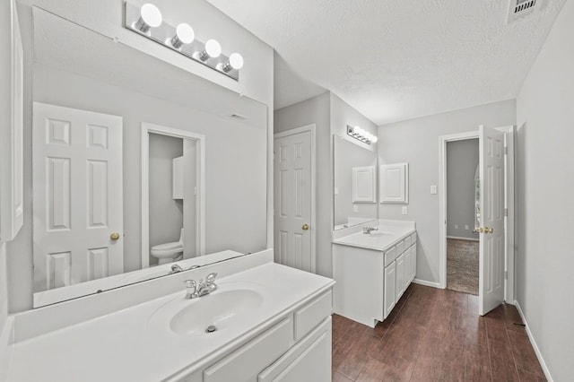 bathroom with wood-type flooring, toilet, large vanity, and a textured ceiling