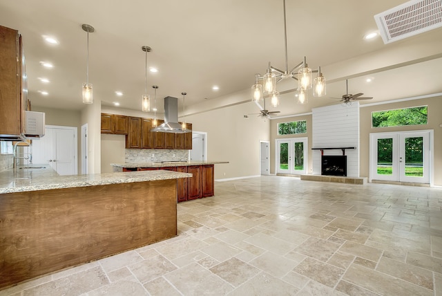 kitchen with light stone counters, ceiling fan, tasteful backsplash, island range hood, and pendant lighting