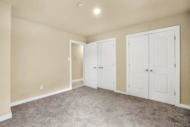 unfurnished bedroom featuring dark carpet and two closets