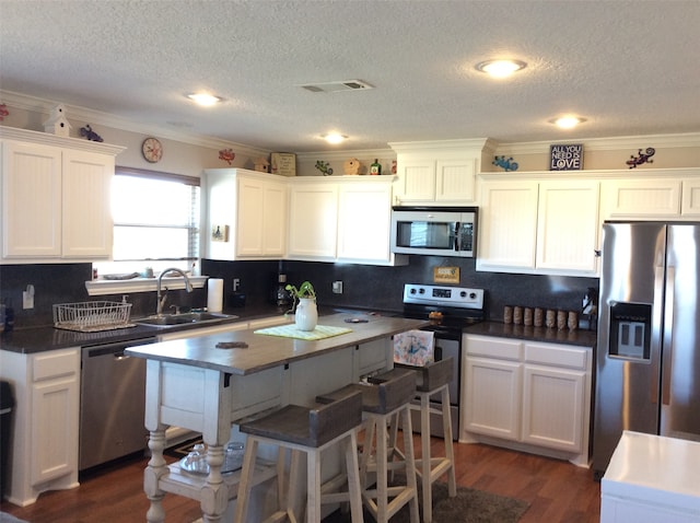 kitchen with a textured ceiling, dark wood-type flooring, ornamental molding, and appliances with stainless steel finishes