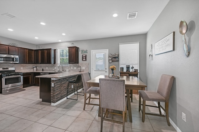 kitchen with backsplash, appliances with stainless steel finishes, dark brown cabinetry, and light tile floors