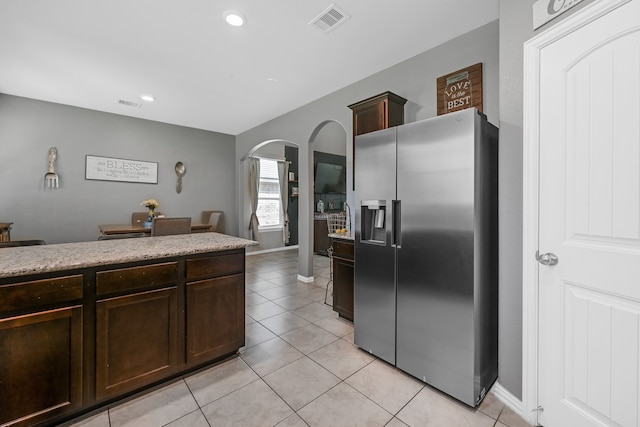 kitchen with light tile flooring, light stone counters, stainless steel fridge, and dark brown cabinetry