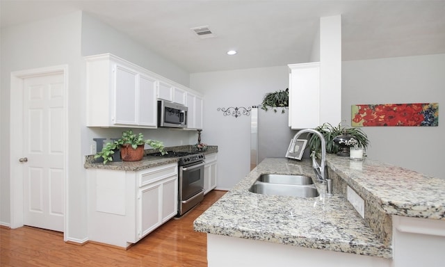 kitchen featuring sink, appliances with stainless steel finishes, kitchen peninsula, light hardwood / wood-style floors, and white cabinets