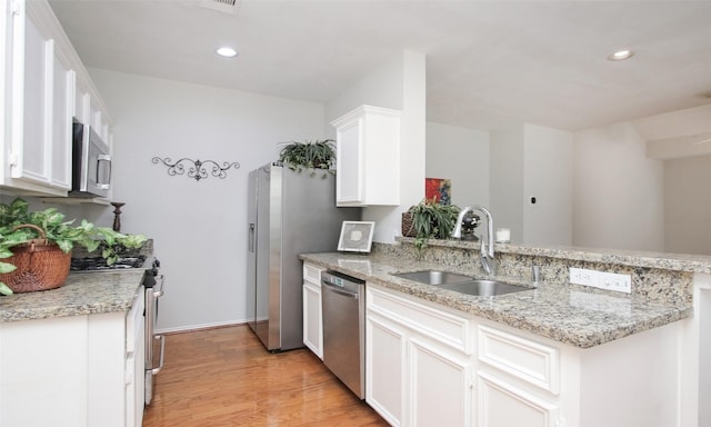 kitchen with sink, appliances with stainless steel finishes, white cabinetry, light stone countertops, and kitchen peninsula