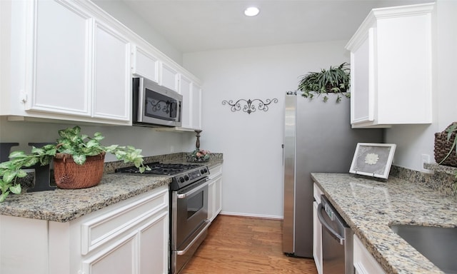 kitchen featuring light stone counters, appliances with stainless steel finishes, light hardwood / wood-style floors, and white cabinets