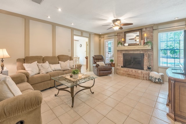 living room with a textured ceiling, ceiling fan, a brick fireplace, light tile patterned flooring, and brick wall