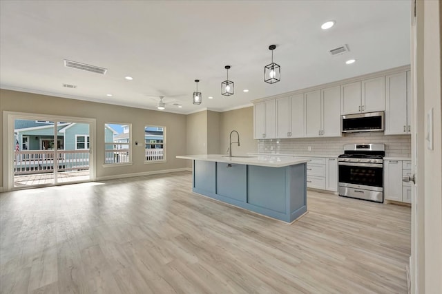 kitchen with appliances with stainless steel finishes, decorative backsplash, pendant lighting, light wood-type flooring, and sink