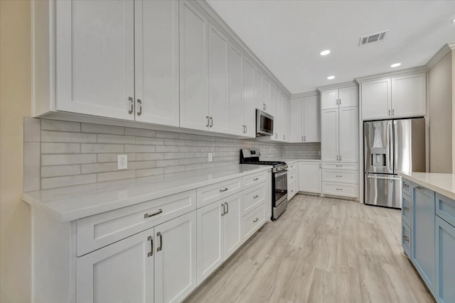 kitchen featuring light hardwood / wood-style floors, white cabinetry, backsplash, blue cabinetry, and stainless steel appliances