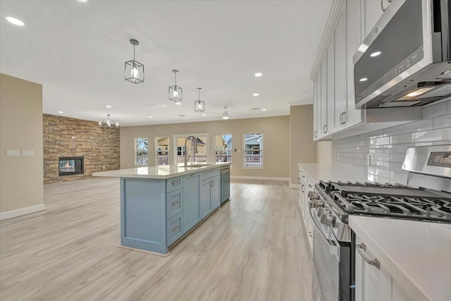 kitchen featuring appliances with stainless steel finishes, hanging light fixtures, decorative backsplash, a kitchen island with sink, and sink