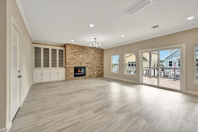 unfurnished living room with a stone fireplace, a notable chandelier, light wood-type flooring, and crown molding