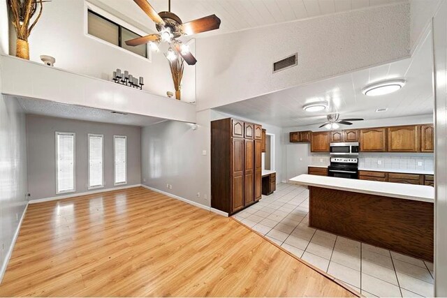 kitchen with tasteful backsplash, a towering ceiling, stainless steel appliances, and light hardwood / wood-style floors