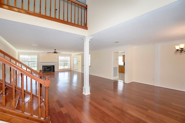 unfurnished living room with ornamental molding, ceiling fan with notable chandelier, ornate columns, and dark wood-type flooring