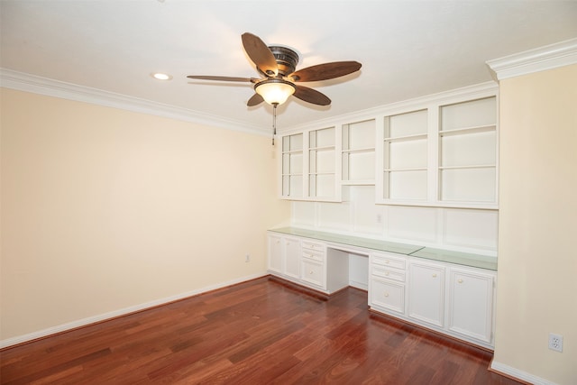 unfurnished office with ceiling fan, built in desk, dark wood-type flooring, and crown molding