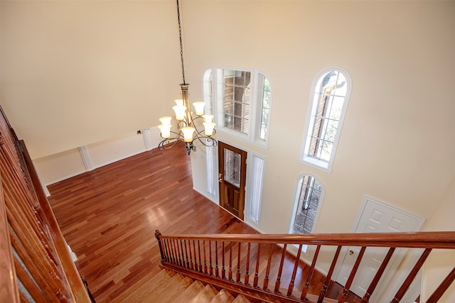 stairs with wood-type flooring, a chandelier, and a towering ceiling