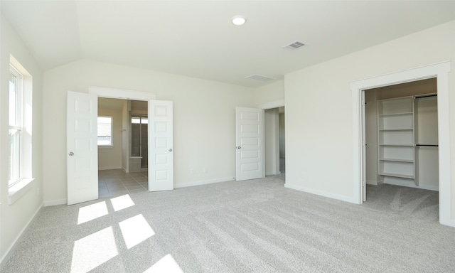 unfurnished bedroom with light carpet, lofted ceiling, a closet, and a walk in closet