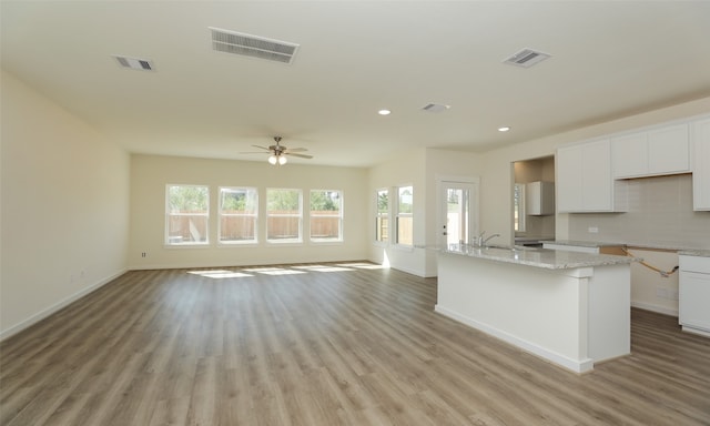 kitchen with ceiling fan, light stone counters, a kitchen island with sink, white cabinetry, and light wood-type flooring