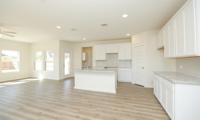 kitchen with light stone countertops, white cabinetry, a kitchen island with sink, and light hardwood / wood-style flooring