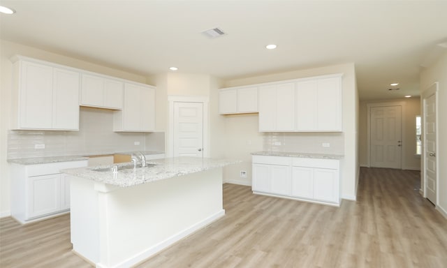 kitchen with an island with sink, white cabinets, sink, and light hardwood / wood-style floors