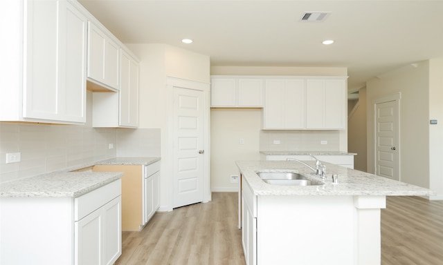 kitchen with light wood-type flooring, a center island with sink, sink, backsplash, and white cabinetry