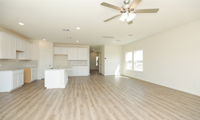 kitchen featuring ceiling fan, an island with sink, light hardwood / wood-style flooring, white cabinetry, and decorative backsplash