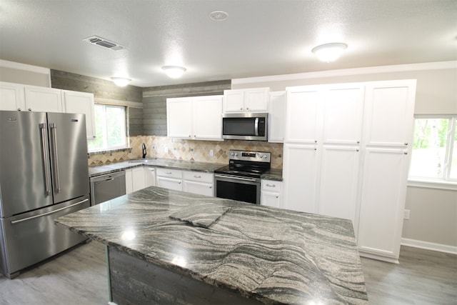 kitchen with a wealth of natural light, appliances with stainless steel finishes, white cabinetry, and light wood-type flooring